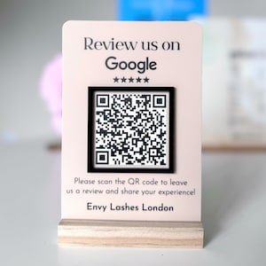 Peut inclure: Une pancarte rose et blanche avec un code QR noir et blanc. La pancarte indique "Review us on Google" et "Please scan the QR code to leave us a review and share your experience!" et "Envy Lashes London".