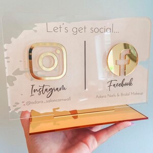 May include: A pink and gold acrylic sign with the text "Let's get social..." and icons for Instagram and Facebook. The Instagram icon has the text "@adara_saloncornwall" and the Facebook icon has the text "Adara Nails & Bridal Makeup".