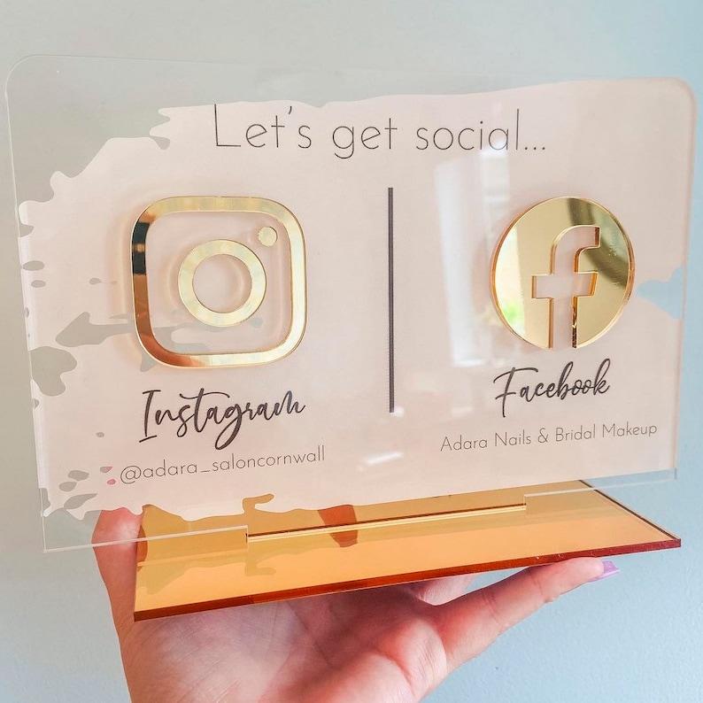 May include: A pink and gold acrylic sign with the text "Let's get social..." and icons for Instagram and Facebook. The Instagram icon has the text "@adara_saloncornwall" and the Facebook icon has the text "Adara Nails & Bridal Makeup".