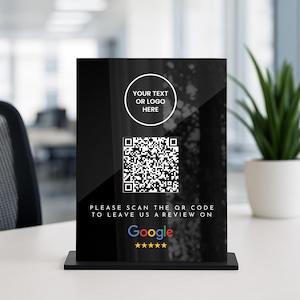 May include: A black acrylic sign featuring a QR code and the Google logo. The sign says "PLEASE SCAN THE QR CODE TO LEAVE US A REVIEW ON Google" and has a space for a logo or text. The Google logo is accompanied by five gold stars.