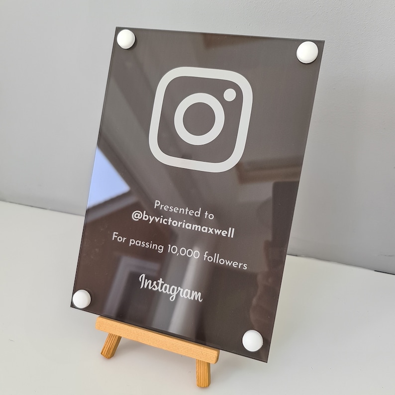 May include: A black acrylic plaque with a white Instagram logo and the text "Presented to @byvictoriamaxwell for passing 10,000 followers Instagram". The plaque is on a small wooden easel.