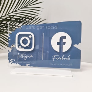 May include: A blue and white acrylic sign with the text "Lets get social..." and the Instagram and Facebook logos. The Instagram logo has the text "Instagram @byvictoriamaxwell" and the Facebook logo has the text "Facebook by victoria maxwell".