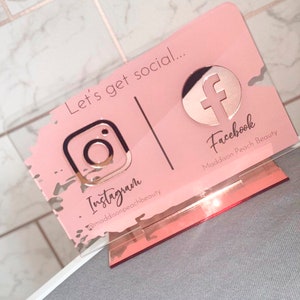 May include: Pink acrylic sign with a rose gold finish. The sign says "Let's get social..." and features the Instagram and Facebook logos with the corresponding social media handles.
