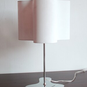 May include: A white table lamp with a unique, wavy, white fabric shade and a chrome base with a three-pronged design.