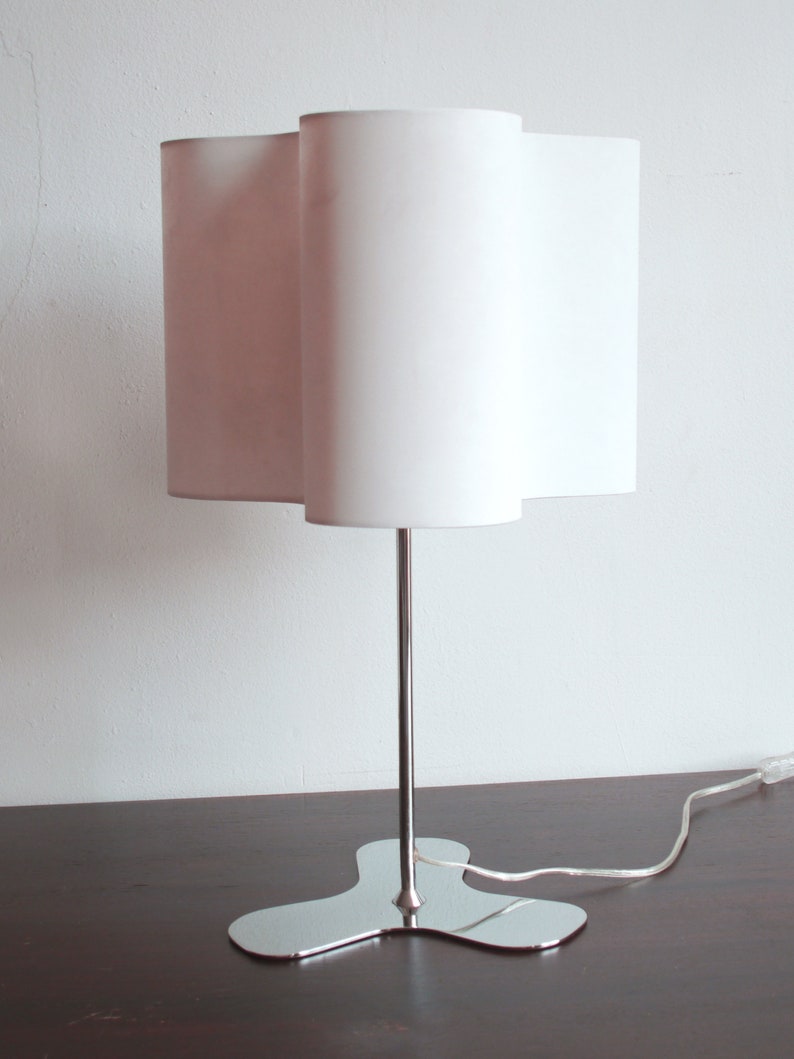 May include: A white table lamp with a unique, wavy, white fabric shade and a chrome base with a three-pronged design.