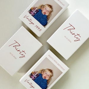 May include: Four white boxes with red text that reads "Thirty" and "10.12.2026". Two boxes have a vintage photo and the text "Vintage 1995". One box reads "Riley's 30th Birthday". The boxes are arranged on a white surface.