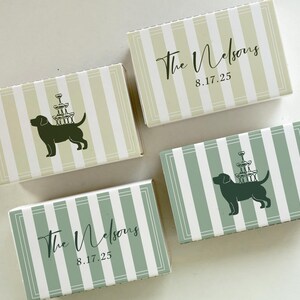 May include: Four rectangular boxes with a striped pattern in green and white. Two boxes have a dog silhouette carrying a champagne glass tower. The other two boxes have the text "The Nelsons" and the date "8.17.25".