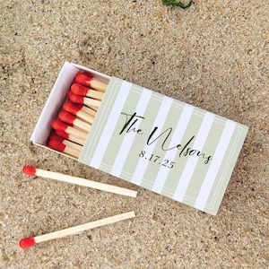 May include: A matchbox with a green and white striped design, featuring the text "The Nelsons" and the date "8.17.25". The box is open, revealing red-tipped matches. Two loose matches are also visible.