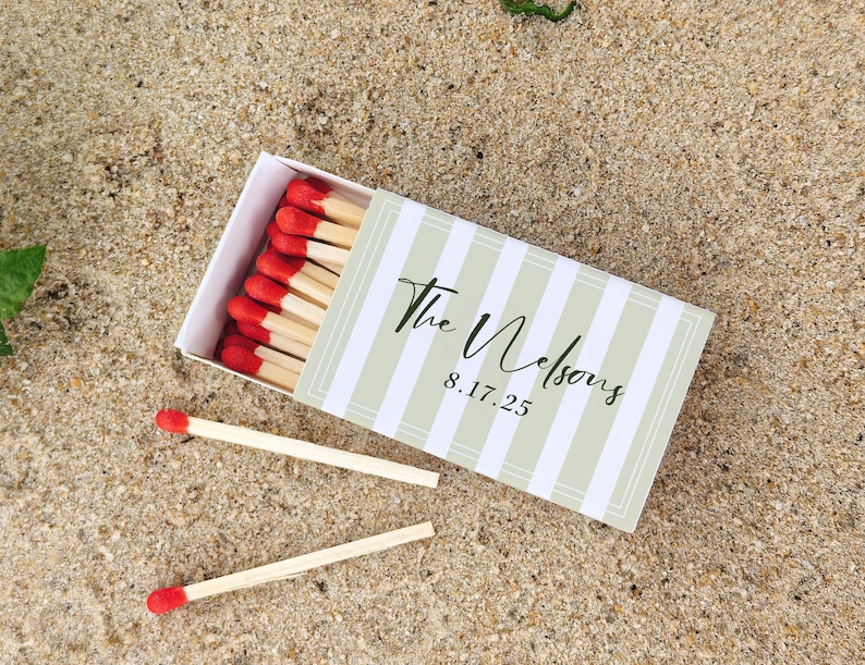 May include: A matchbox with a green and white striped design, featuring the text "The Nelsons" and the date "8.17.25". The box is open, revealing red-tipped matches. Two loose matches are also visible.