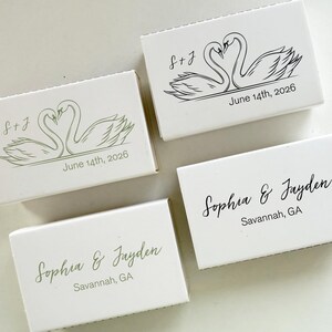 May include: Four white matchboxes with custom text and swan illustrations. Two boxes feature the names "Sophia & Jayden" and "Savannah, GA". The other two boxes have swan graphics and the text "S+J" and "June 14th, 2026".