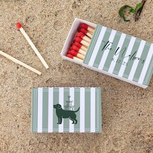 May include: Matchboxes with a green and white striped design. One box is open, revealing red-tipped matches. The top box has the text "The Nelsons" and the date "8.17.25". The bottom box features a dog silhouette with a champagne tower.