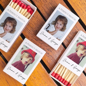 May include: Four matchboxes with custom photos and text on a wooden surface. The boxes read "A PERFECT MATCH" and "Emma & Geroge". Two boxes are open, revealing red-tipped matches.