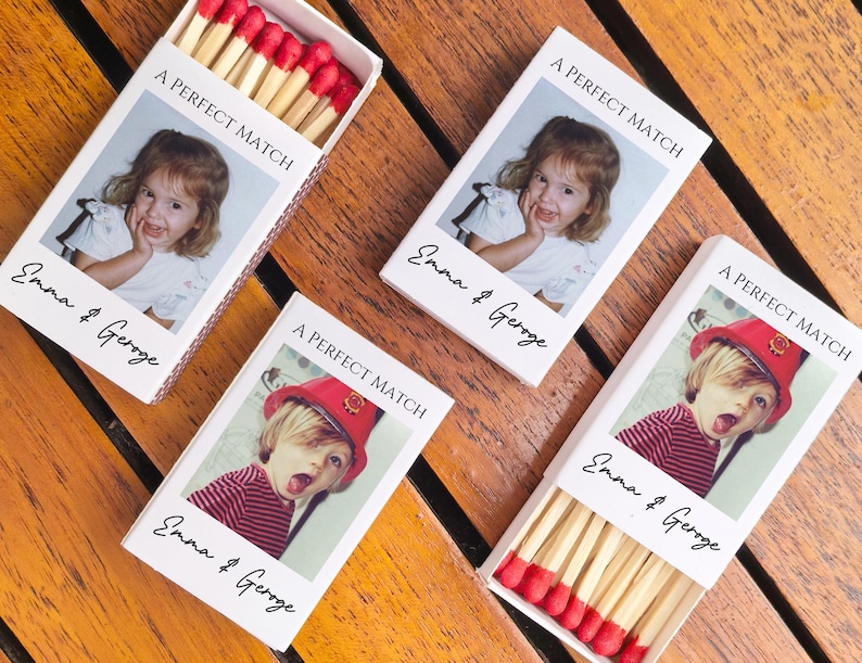 May include: Four matchboxes with custom photos and text on a wooden surface. The boxes read "A PERFECT MATCH" and "Emma & Geroge". Two boxes are open, revealing red-tipped matches.