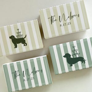 May include: Four rectangular boxes with striped patterns in green and white. Two boxes feature a dog silhouette with champagne glasses, and the other two have the text "The Nelsons 8.17.25" in elegant script. The boxes are likely for a wedding or special event.