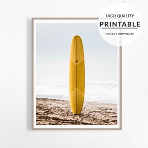 May include: A yellow surfboard standing upright on a sandy beach with a light blue sky and white clouds in the background.