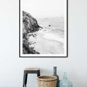 Puede incluir: Fotograf&iacute;a en blanco y negro de un acantilado rocoso con vistas a una playa de arena y el oc&eacute;ano. La foto est&aacute; enmarcada en un marco negro.