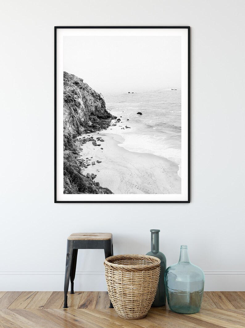 Puede incluir: Fotograf&iacute;a en blanco y negro de un acantilado rocoso con vistas a una playa de arena y el oc&eacute;ano. La foto est&aacute; enmarcada en un marco negro.