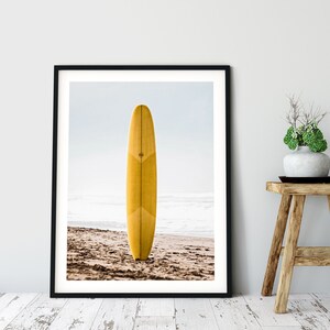 May include: A yellow surfboard standing upright on a sandy beach with the ocean in the background.