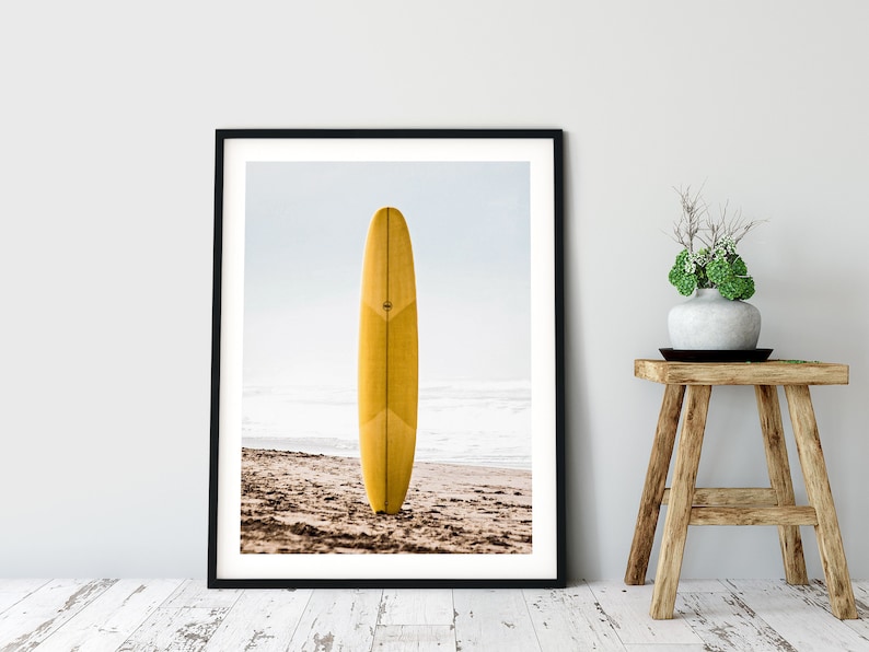 May include: A yellow surfboard standing upright on a sandy beach with the ocean in the background.