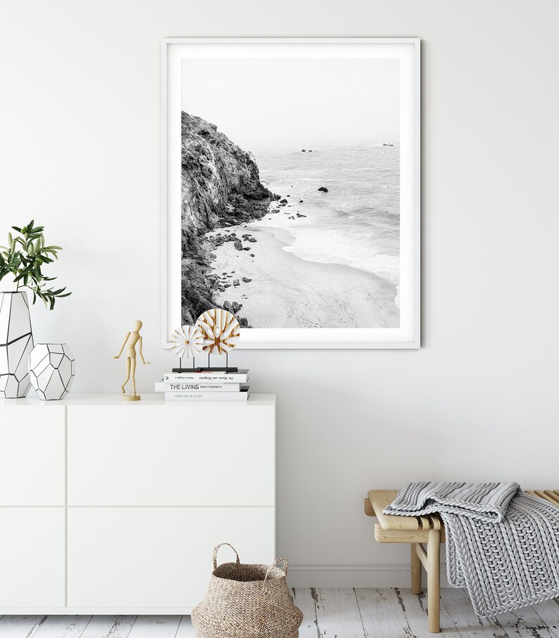 Puede incluir: Fotograf&iacute;a en blanco y negro de una costa rocosa con una playa de arena y olas del oc&eacute;ano. La foto est&aacute; enmarcada en un marco blanco y colgada en una pared blanca.