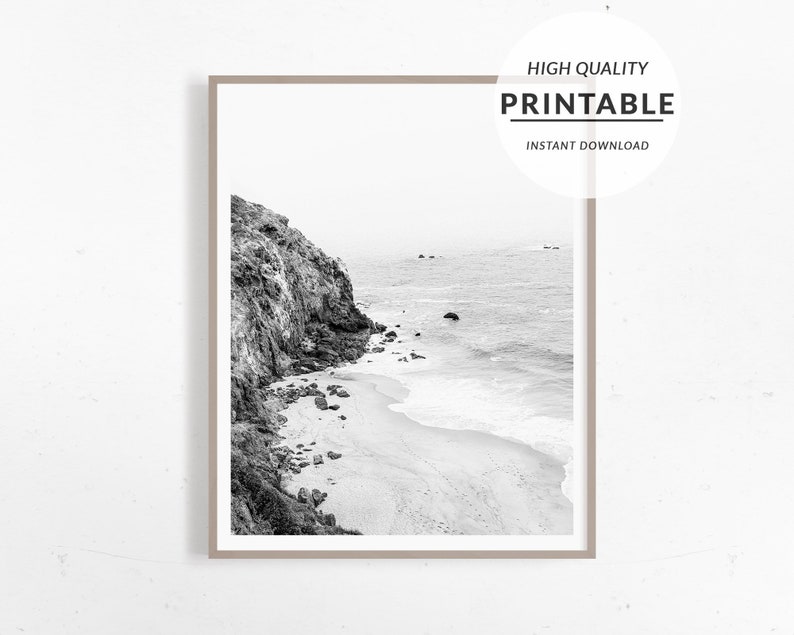 Puede incluir: Fotograf&iacute;a en blanco y negro de un acantilado rocoso que domina una playa de arena con olas rompiendo en la orilla.