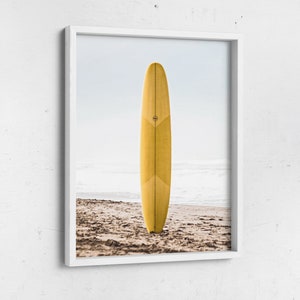 May include: A yellow surfboard standing upright on a sandy beach with the ocean in the background.