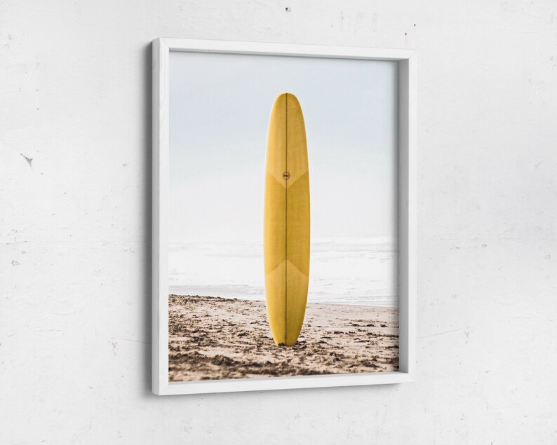 May include: A yellow surfboard standing upright on a sandy beach with the ocean in the background.