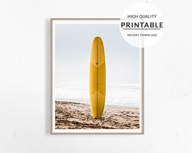 May include: A yellow surfboard standing upright on a sandy beach with a light blue sky and white clouds in the background.