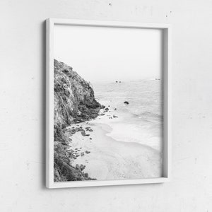 Puede incluir: Fotograf&iacute;a en blanco y negro de un acantilado rocoso que se encuentra con una playa de arena con olas rompiendo en la orilla.