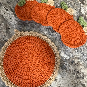 May include: Set of six crocheted pumpkin-shaped coasters in orange with green stems and a larger crocheted orange coaster with a brown border.