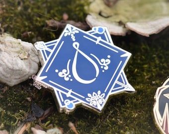 May include: A blue and silver enamel pin with a white stylized letter 'S' in a square frame. The pin has a decorative border with floral details and blue accents.