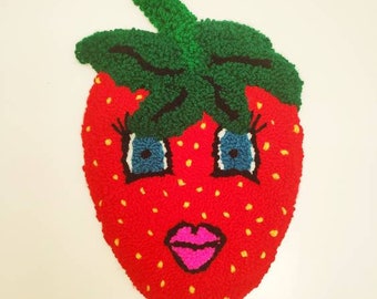 May include: A red strawberry with a yellow seed pattern and a green leafy top. The strawberry has a cartoon face with blue eyes, black eyelashes, and a pink open mouth.