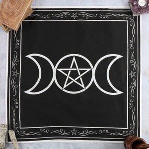 May include: Square black altar cloth with a white triple moon and pentagram design. The border is white, decorated with stars and swirls. The cloth is made of dark fabric and is suitable for spiritual practices.