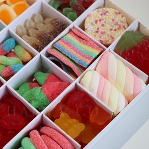 Puede incluir: Una caja blanca llena de una variedad de caramelos coloridos. El surtido incluye caramelos de goma, tiras de arco&iacute;ris, dulces con forma de fresa y malvaviscos. Los caramelos est&aacute;n dispuestos en compartimentos individuales.