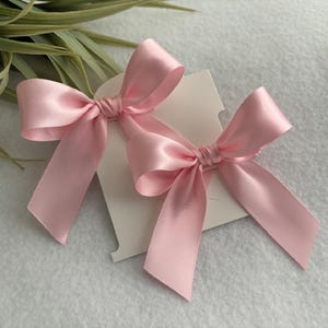 May include: Two pink satin bows tied together with a white card behind them.