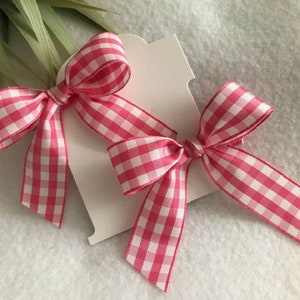 May include: Two pink and white gingham ribbon bows tied together. The bows are on a white card.