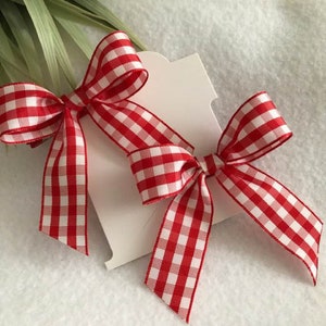 May include: Two red and white gingham ribbon bows tied together. The bows are tied on a white card.