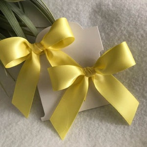 May include: Two yellow satin ribbon bows tied together on a white card.