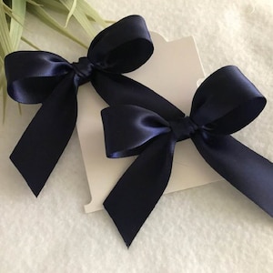 May include: Two navy blue satin ribbon bows. The bows are tied with a simple knot and have a classic, elegant look.