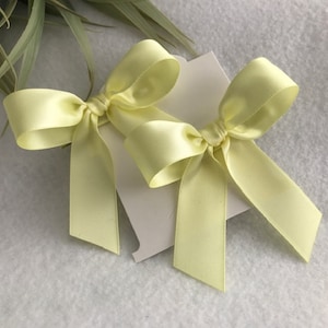 May include: Two pale yellow satin bows tied together on a white background.