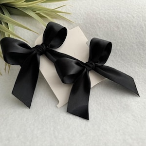 May include: Two black satin ribbon bows tied together. The bows are on a white background.