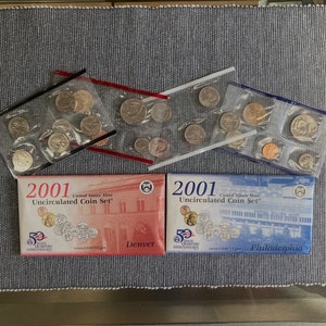 May include: Two 2001 United States Mint Uncirculated Coin Sets, one from Denver and one from Philadelphia. Each set is packaged in a clear plastic bag with the coins inside. The sets are on a grey textured surface.