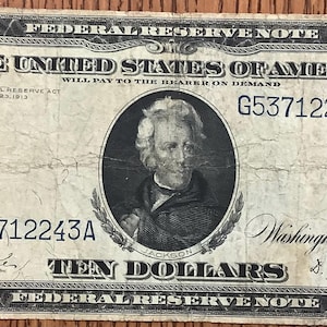 Peut inclure: Un billet de dix dollars de la Réserve fédérale vintage. Le billet présente un portrait d'Andrew Jackson et le texte "TEN DOLLARS". Le billet a un design noir et blanc avec des détails complexes et le texte "THE UNITED STATES OF AMERICA."