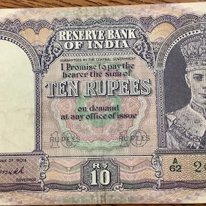May include: A vintage ten rupee note from the Reserve Bank of India. The note features a portrait of a man wearing a crown and ornate clothing. The text includes "TEN RUPEES" and "Reserve Bank of India". The note has a serial number and is in shades of green, pink, and brown.
