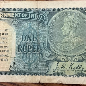 May include: An antique Government of India one rupee note. The note features text in multiple languages, a portrait of King George V, and the text "ONE RUPEE". The note is aged with visible wear and tear.