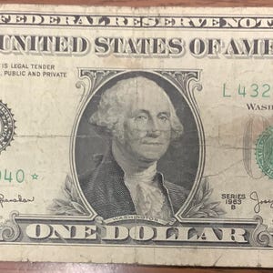 May include: A United States one-dollar Federal Reserve Note featuring a portrait of George Washington in the center. The bill displays the text THE UNITED STATES OF AMERICA, ONE DOLLAR, and serial number L43281040 with a star symbol at the end.