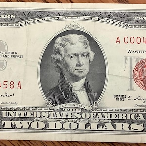 May include: A vintage two-dollar bill featuring a portrait of Thomas Jefferson. The bill has a red seal and serial numbers, with the text "TWO DOLLARS" prominently displayed. The bill is in good condition.