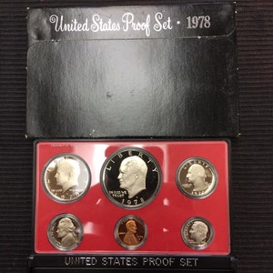 May include: A red and black coin collection case with the text "United States Proof Set 1978" on the front. The case contains a set of eight silver and copper coins from 1978.