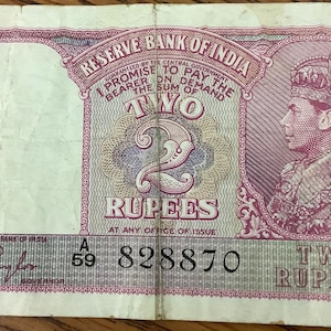 May include: A vintage two-rupee banknote from the Reserve Bank of India. The note features a portrait of a man wearing a crown, with text in English. The note has a green and pink border and the number "2" is prominently displayed.