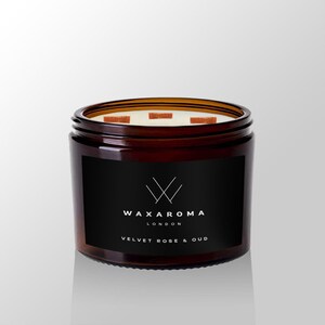 May include: A brown glass jar candle with a black label that says "WAXAROMA LONDON" and "VELVET ROSE & OUD". The candle has a white wax top with three wooden wicks.